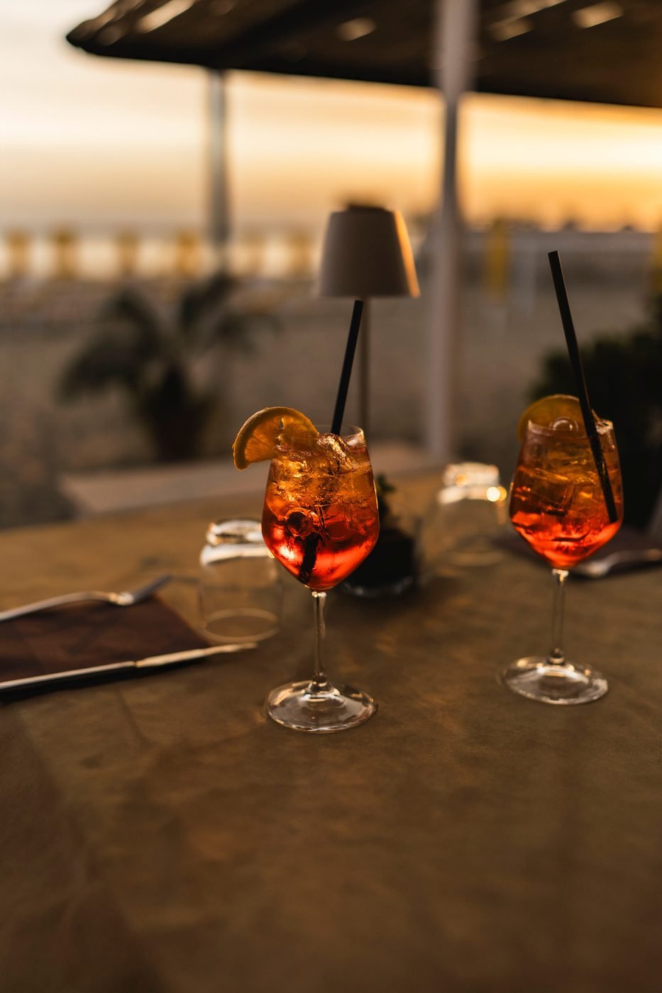 Two spritz glasses at sunset with the beach umbrellas behind
