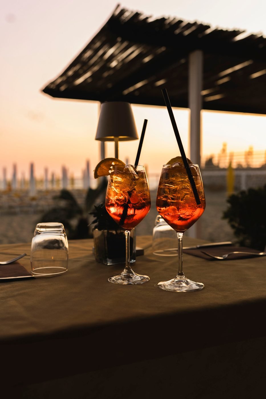 Two spritz on a table under the pergola at sunset, the beach behind